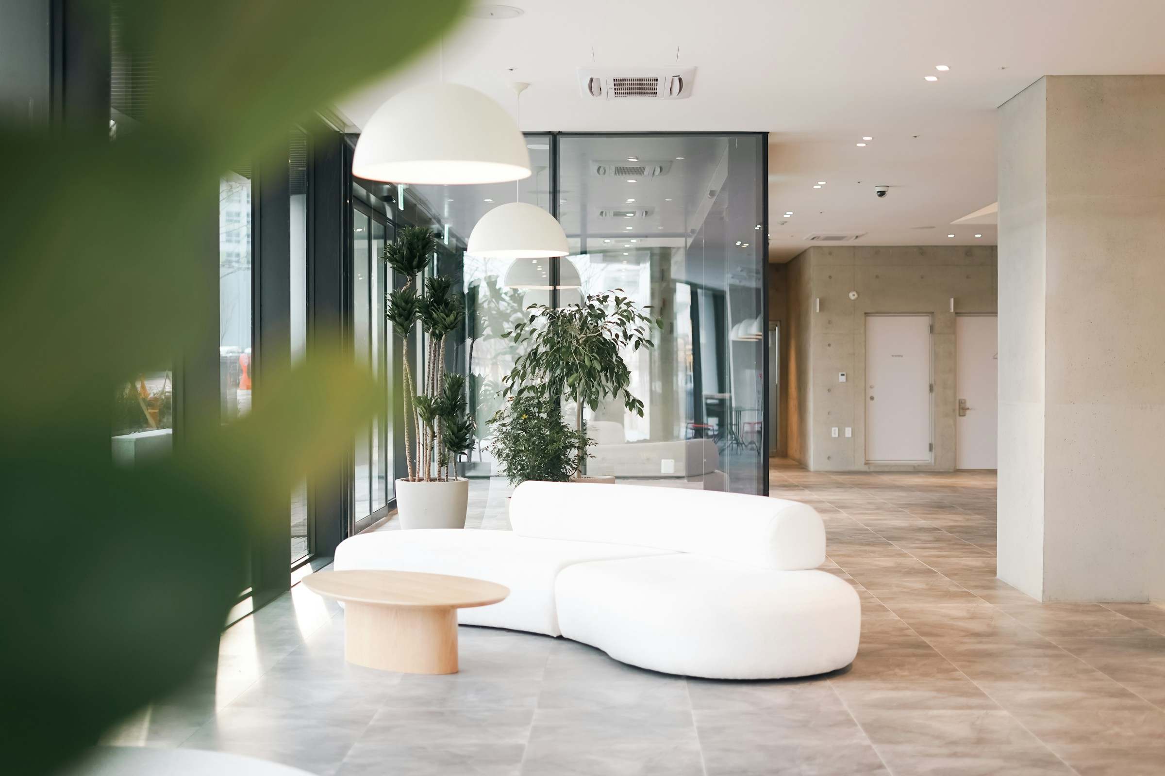 A bright, calm reception area with a white sofa, pale stone floor and indoor plants